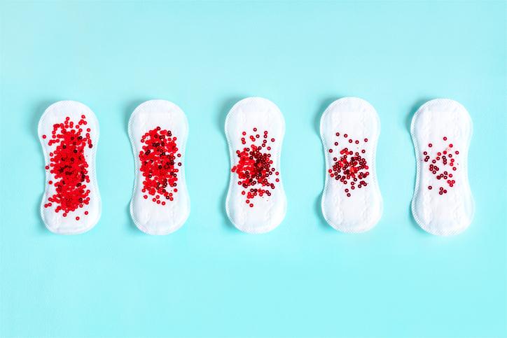 Two menstrual pads with red glitter on blue colored background. Minimalist still life photography concept